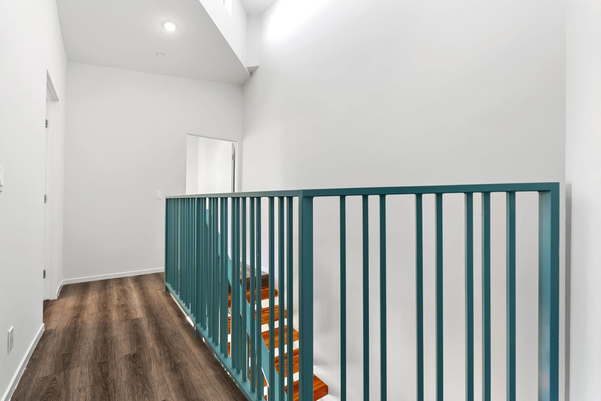 Bright upstairs hallway with teal railing, white walls, and wood flooring.