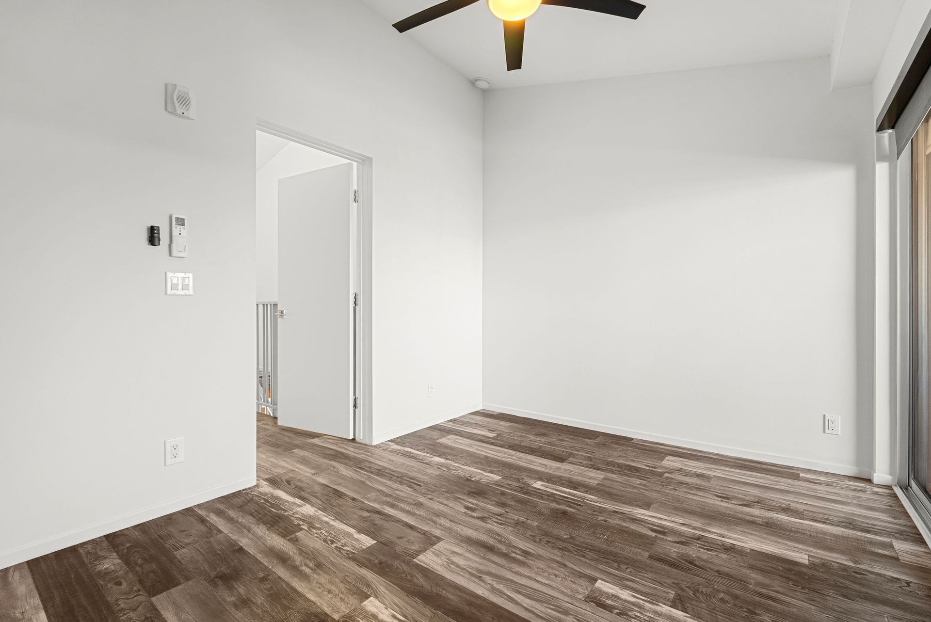 Empty room with wood-look floor, white walls, open door, ceiling fan, and window.