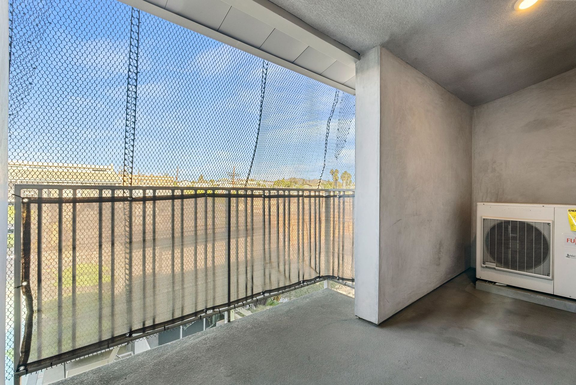 Balcony with metal railing, mesh screen, and white appliance against a textured gray wall.