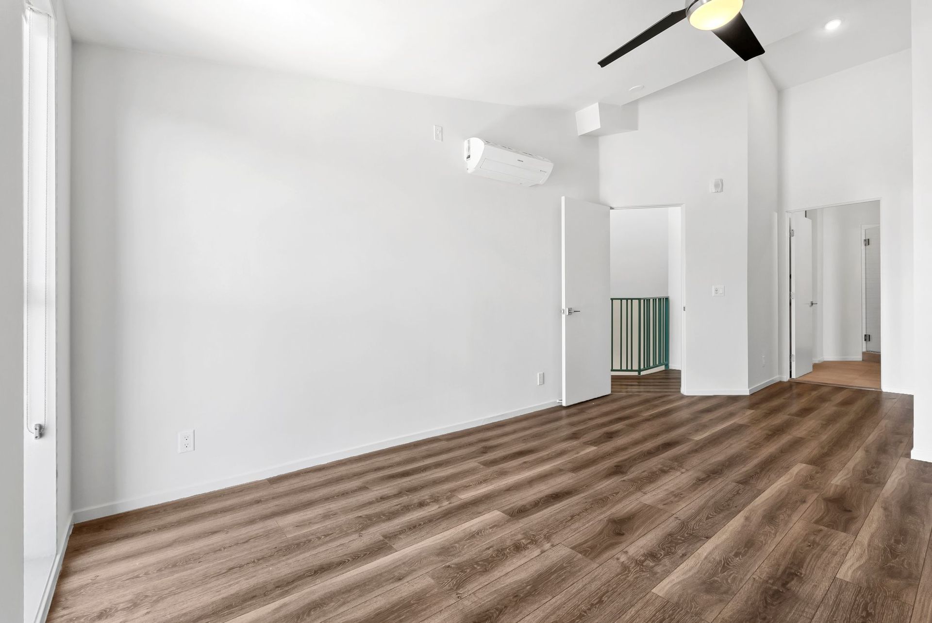 Empty white room with wood-look flooring, recessed lights, and a black ceiling fan.