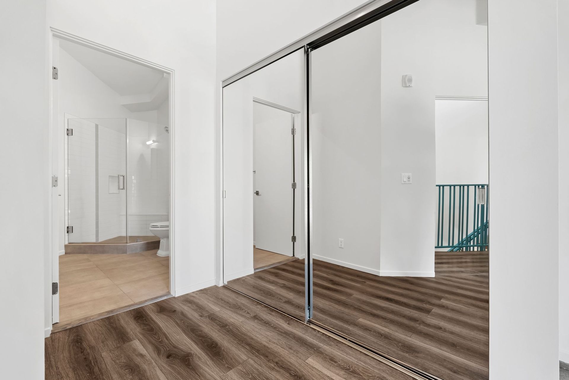 Empty white room with sliding mirrored closet doors and wood-look flooring