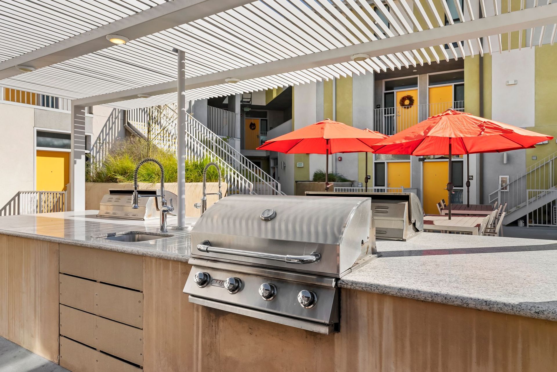 Outdoor patio with stainless grill, stone counter, and red umbrellas beside a modern house