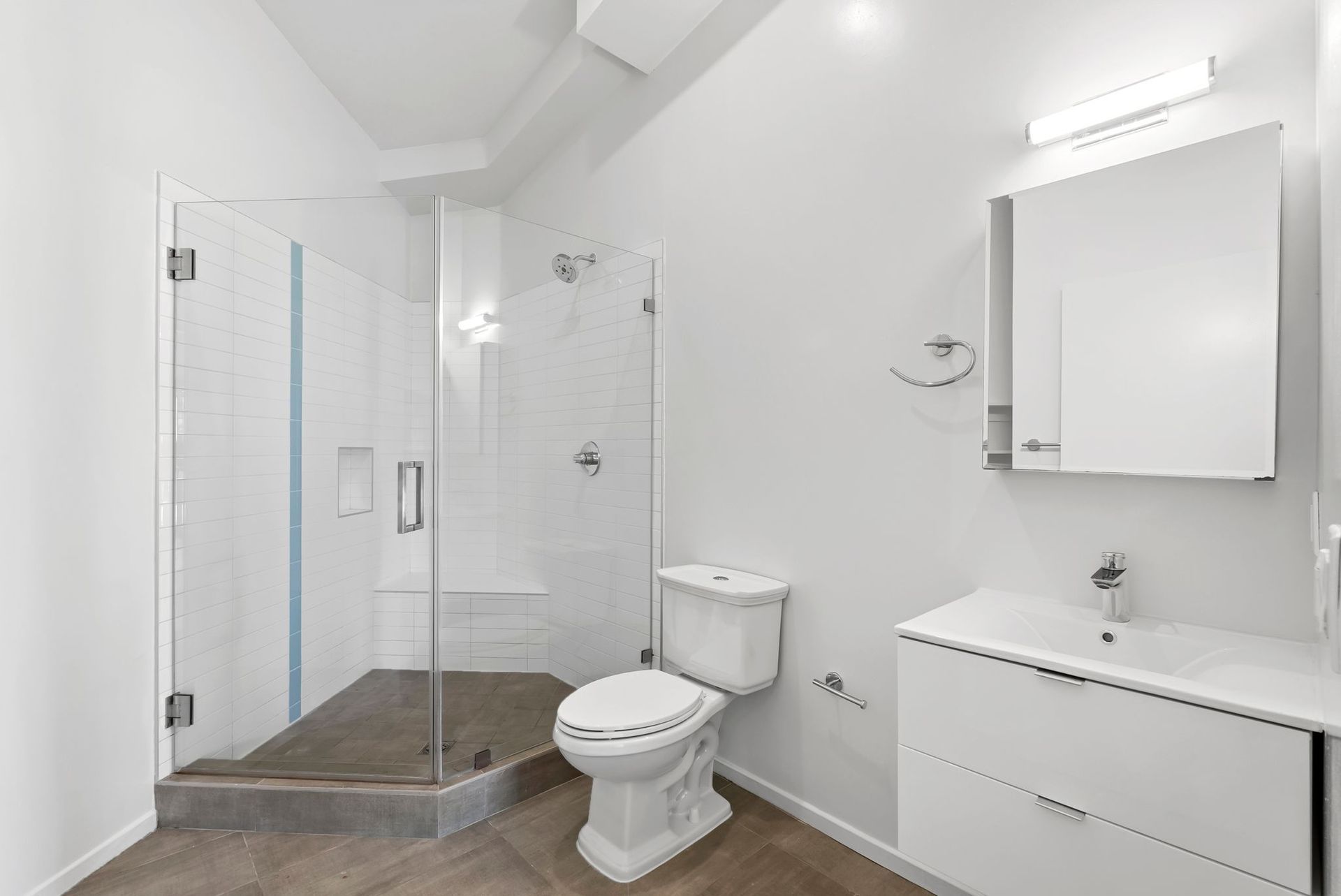 Modern white bathroom with glass shower, toilet, vanity, and mirror cabinet