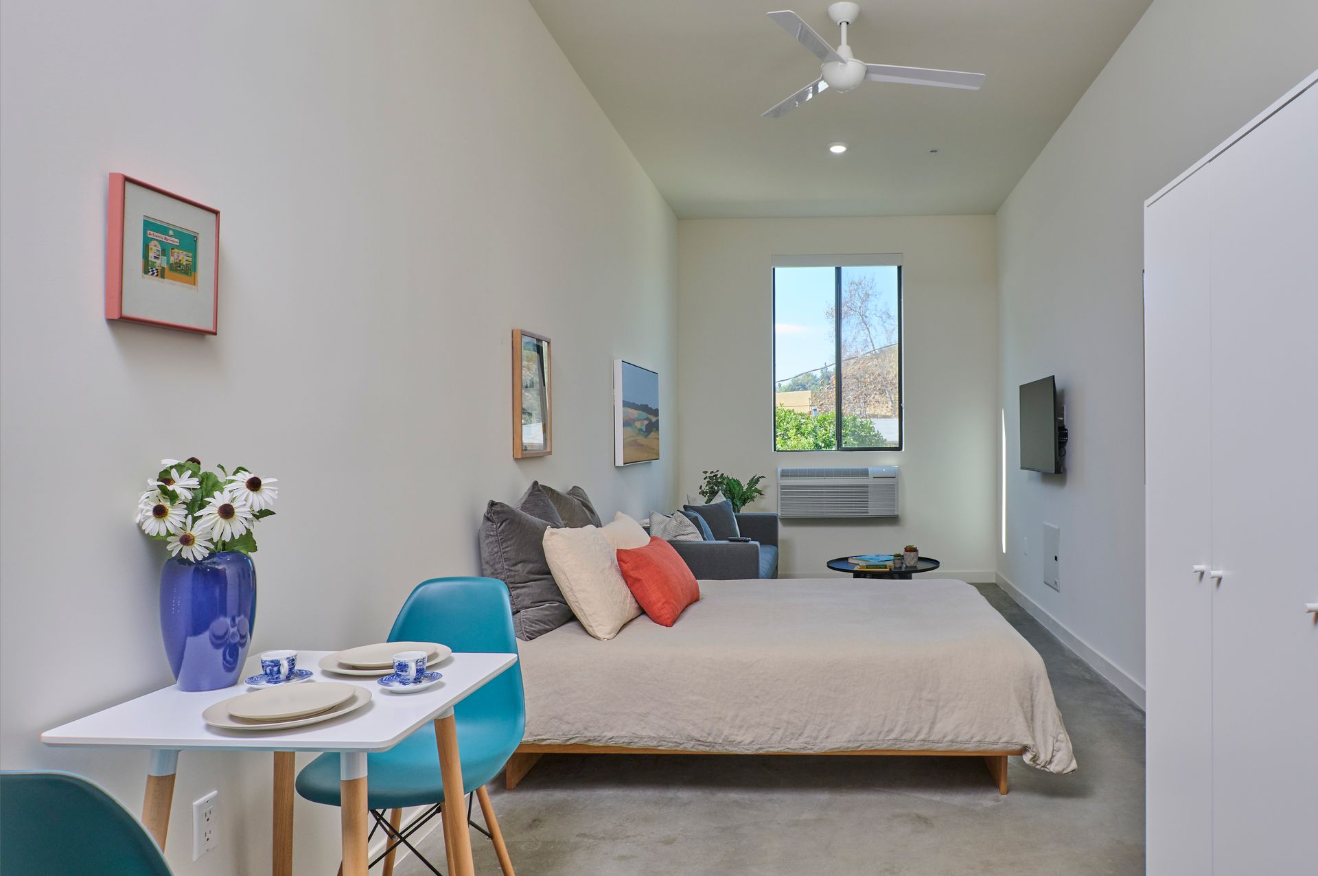 A bedroom with a bed , table , chairs and a ceiling fan.