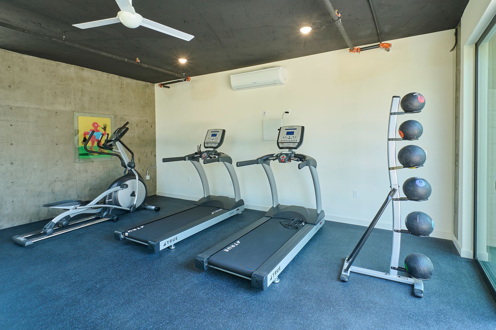 A gym with treadmills , ellipticals , and a ceiling fan.