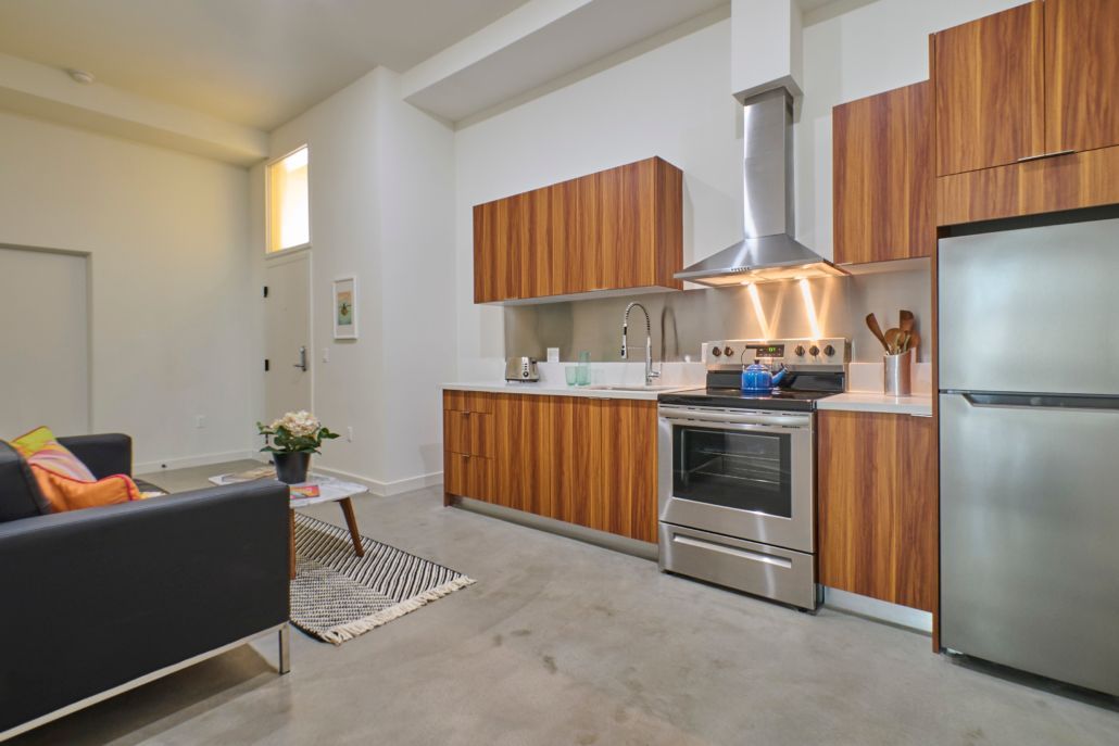 A living room with a couch and a kitchen with stainless steel appliances.