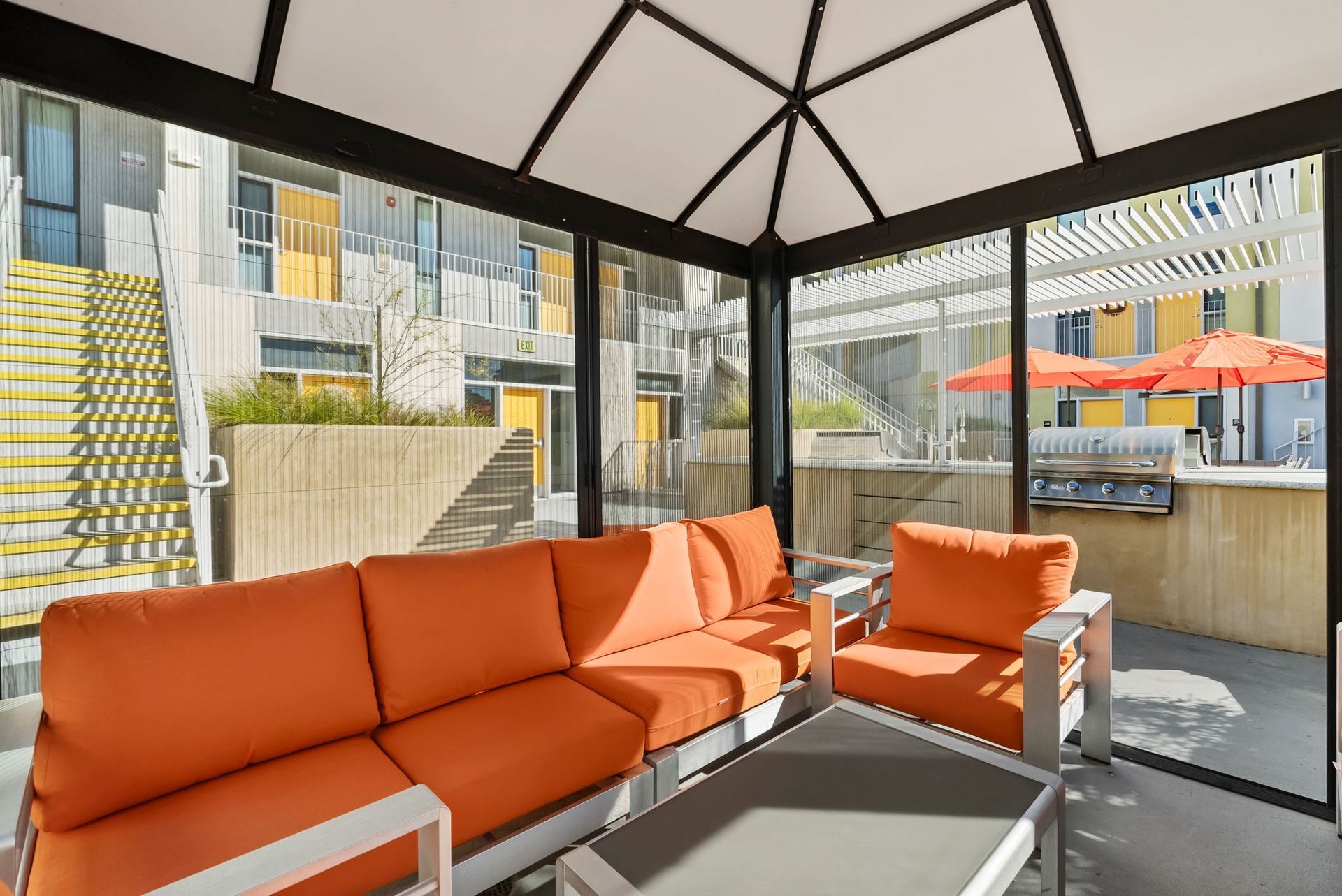 Orange cushioned patio seating under a gazebo with city buildings and outdoor umbrellas in the background