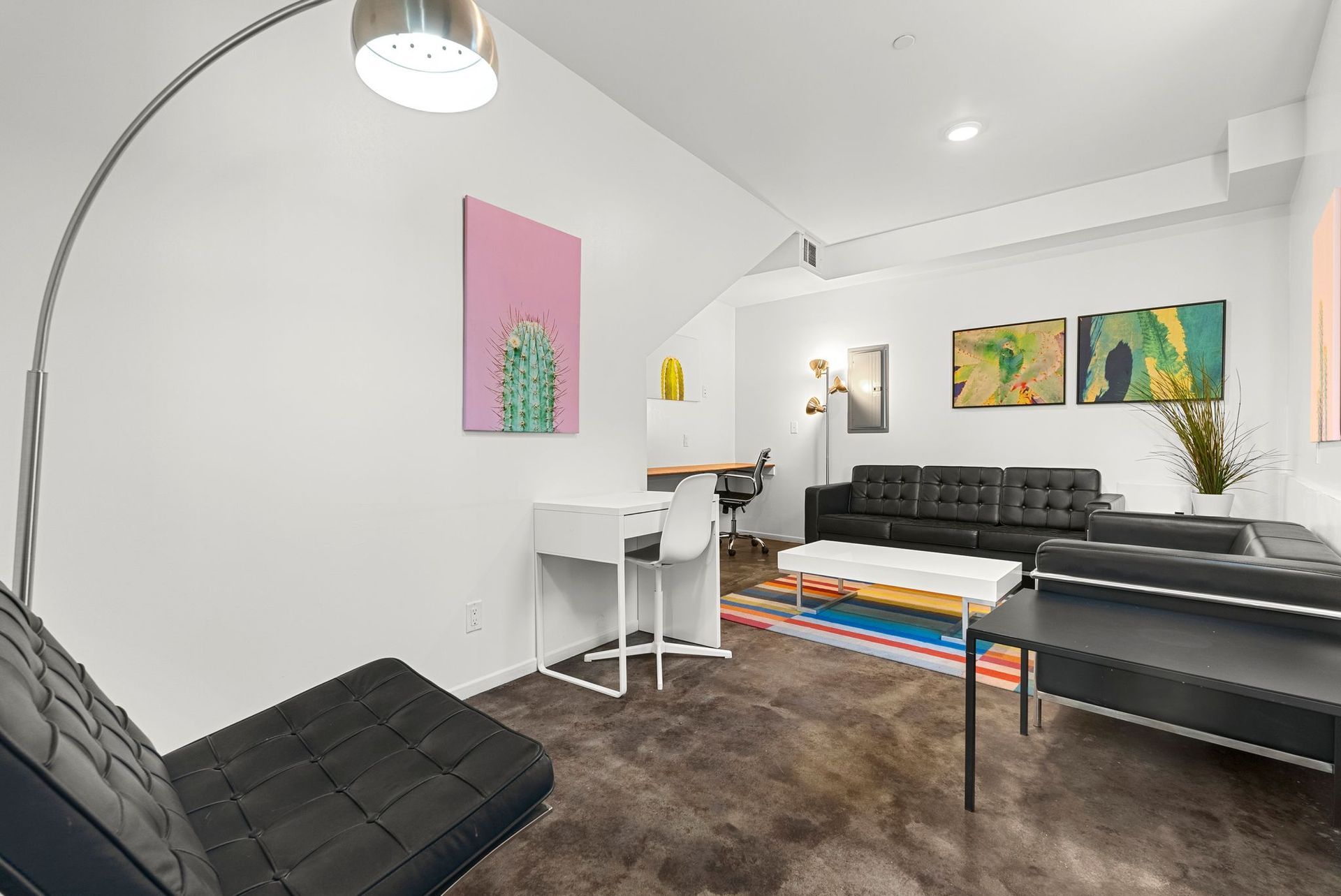 Modern, minimalist living space with black furniture, artwork, and a white desk.