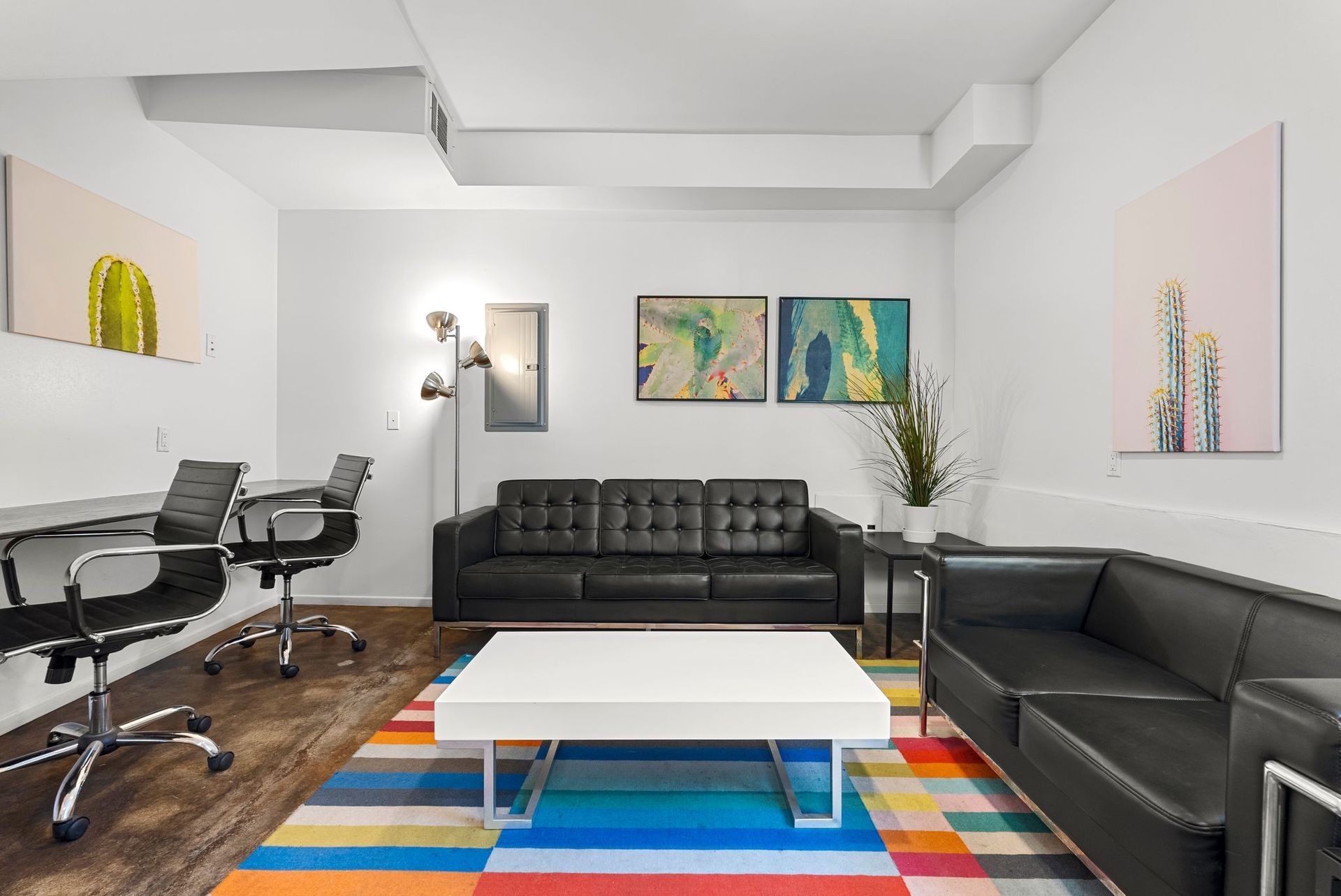 Modern office lounge with black leather couches, colorful rug, white coffee table, artwork.