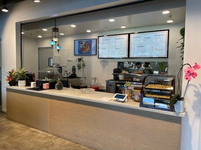 Modern café counter with menu boards, pastry case, coffee equipment, and pink orchids