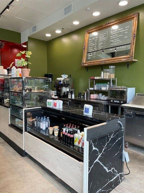 Cafe counter with glass display cases, menu board, and coffee equipment in a green interior