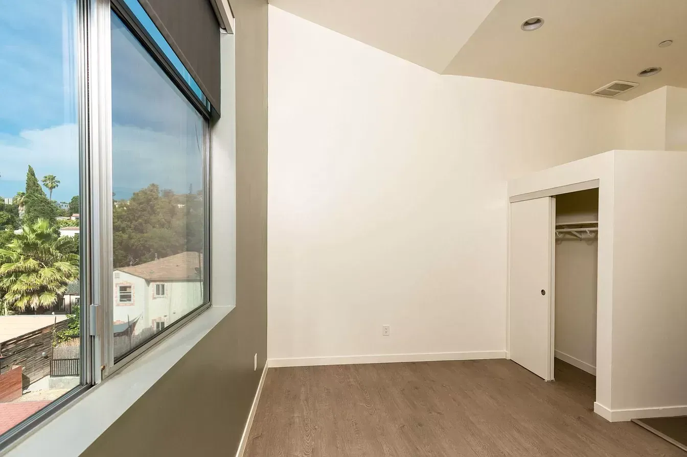 An empty bedroom with a large window and a closet.
