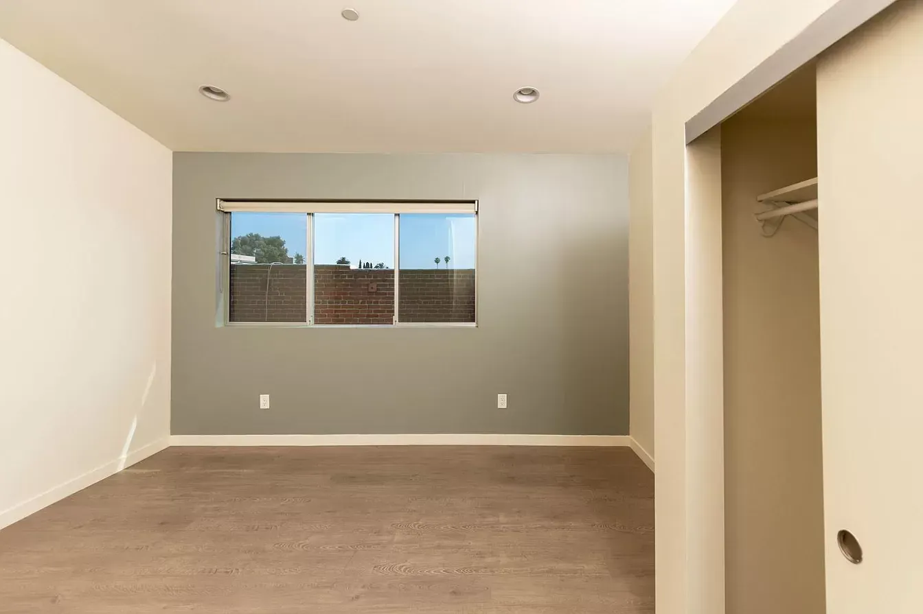 An empty bedroom with a window and a closet.