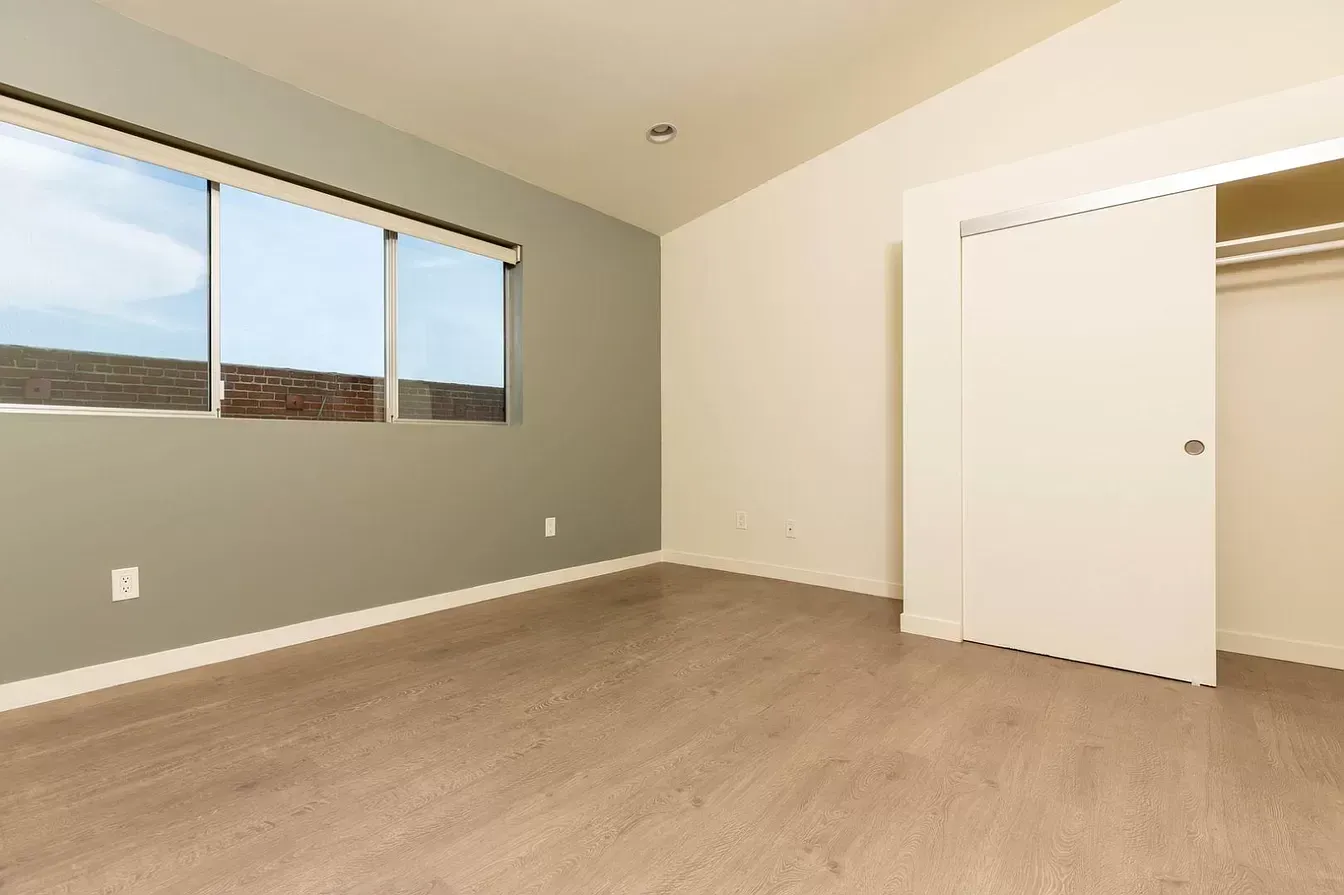 An empty bedroom with a window and a closet.