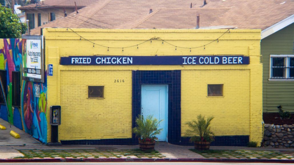 Yellow corner storefront with blue trim, signs for fried chicken and ice cold beer, and colorful mural on the left