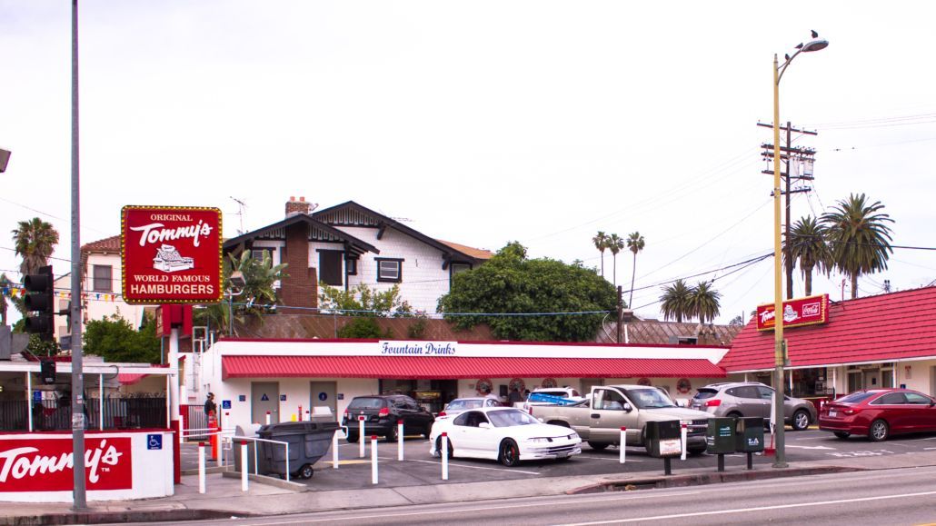 Street view of a red-roofed convenience store with parked cars and palm trees on a cloudy day