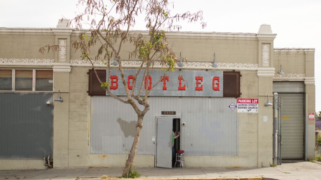 Dilapidated storefront with red lettering above a closed metal door and gray facade, tree in front.