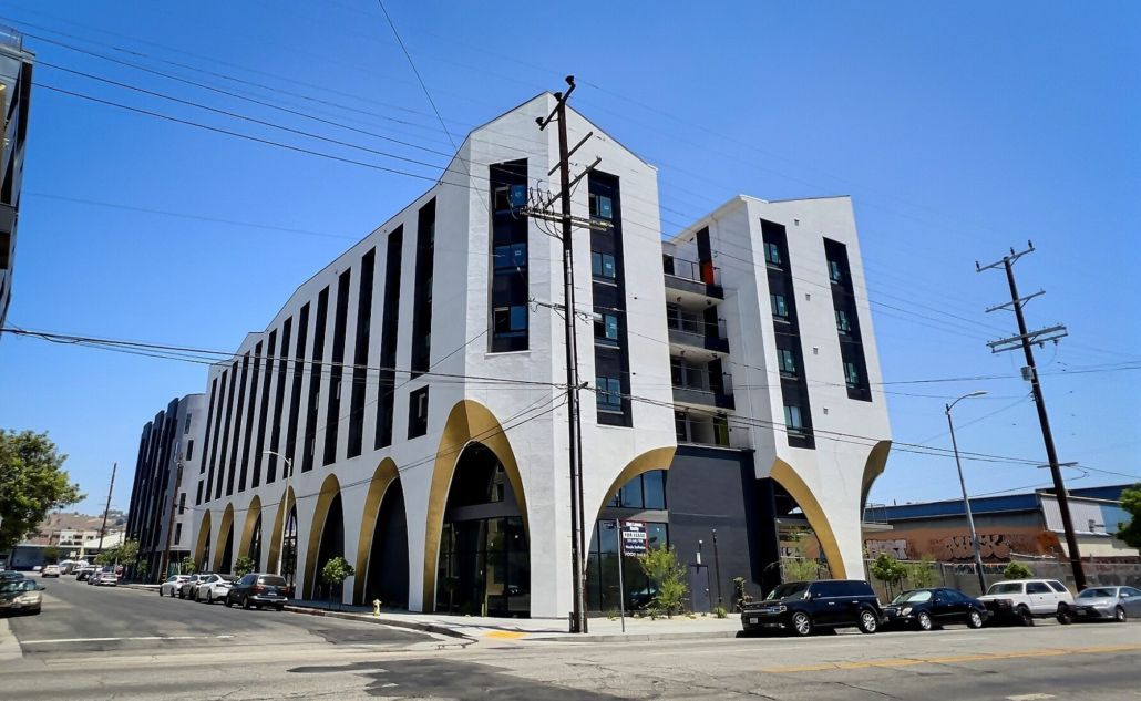 Modern white multi-story building with arched entrances on a sunny street corner