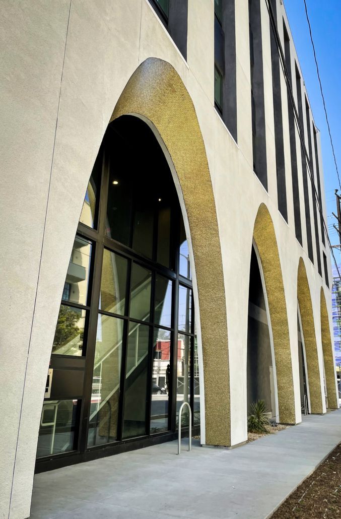 Modern building facade with tall arched windows and beige stone trim along a sidewalk