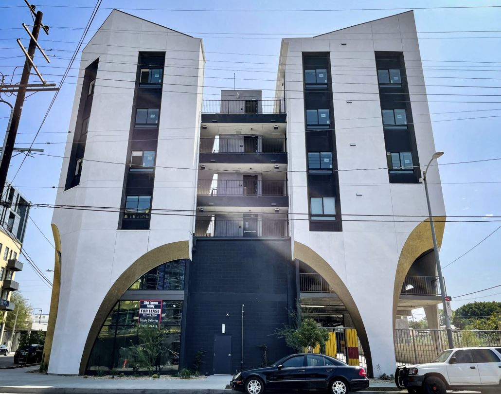 Modern white apartment building with arched ground floor and balconies, viewed from the street