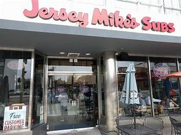 Jersey Mike's Subs storefront with glass doors, a sign, and outdoor seating.