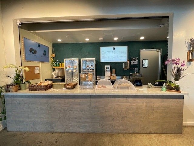 Restaurant counter with pastries, drink dispensers, and a digital menu board behind glass.