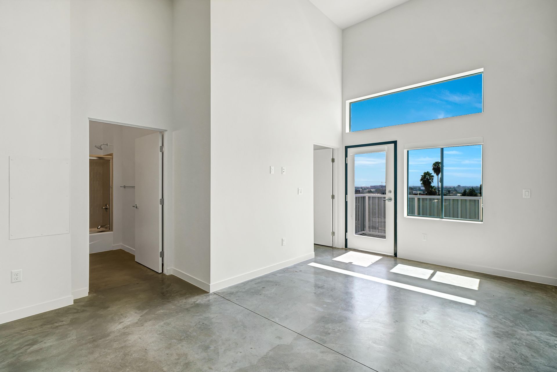 Empty room with concrete floor, white walls, tall windows, and a doorway.