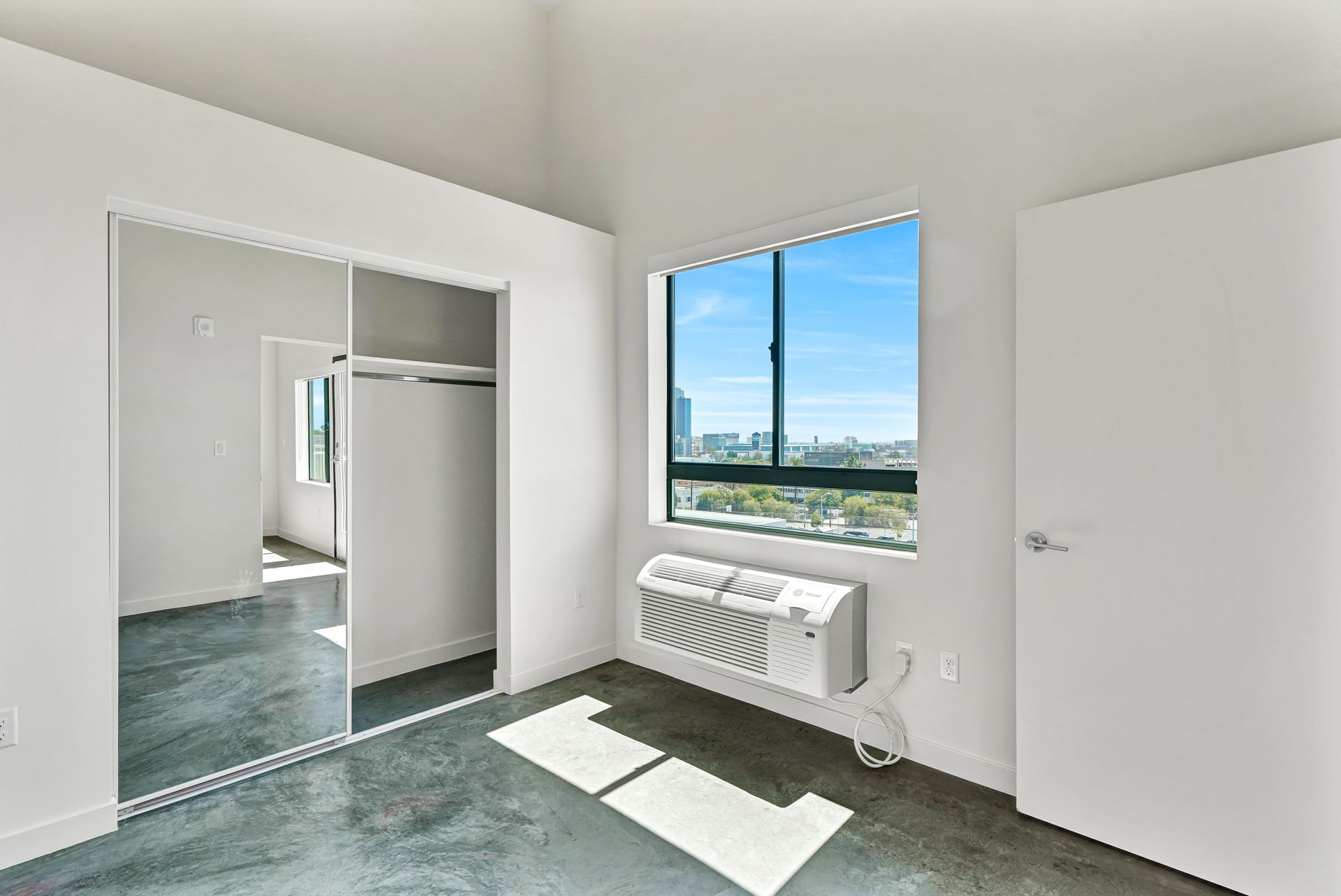 Empty room with large window, closet, and a concrete floor.