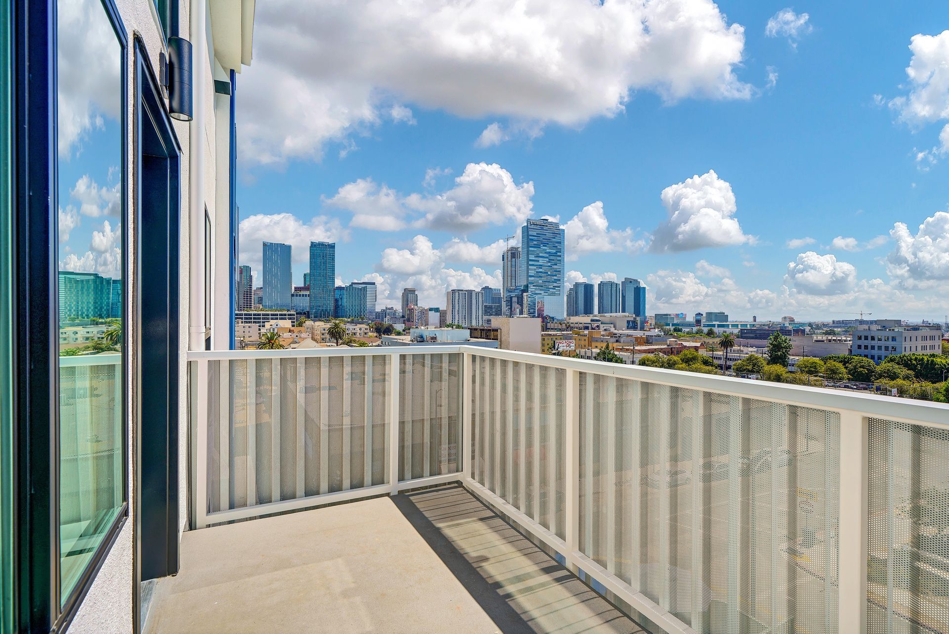 Balcony with white railing overlooking a city skyline on a sunny day.