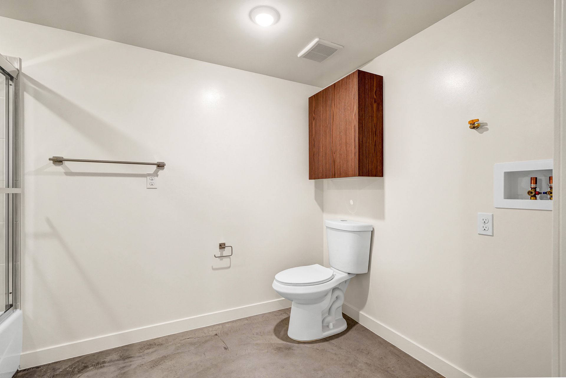 Bathroom with toilet, brown cabinet, towel rack, shower, and white walls.