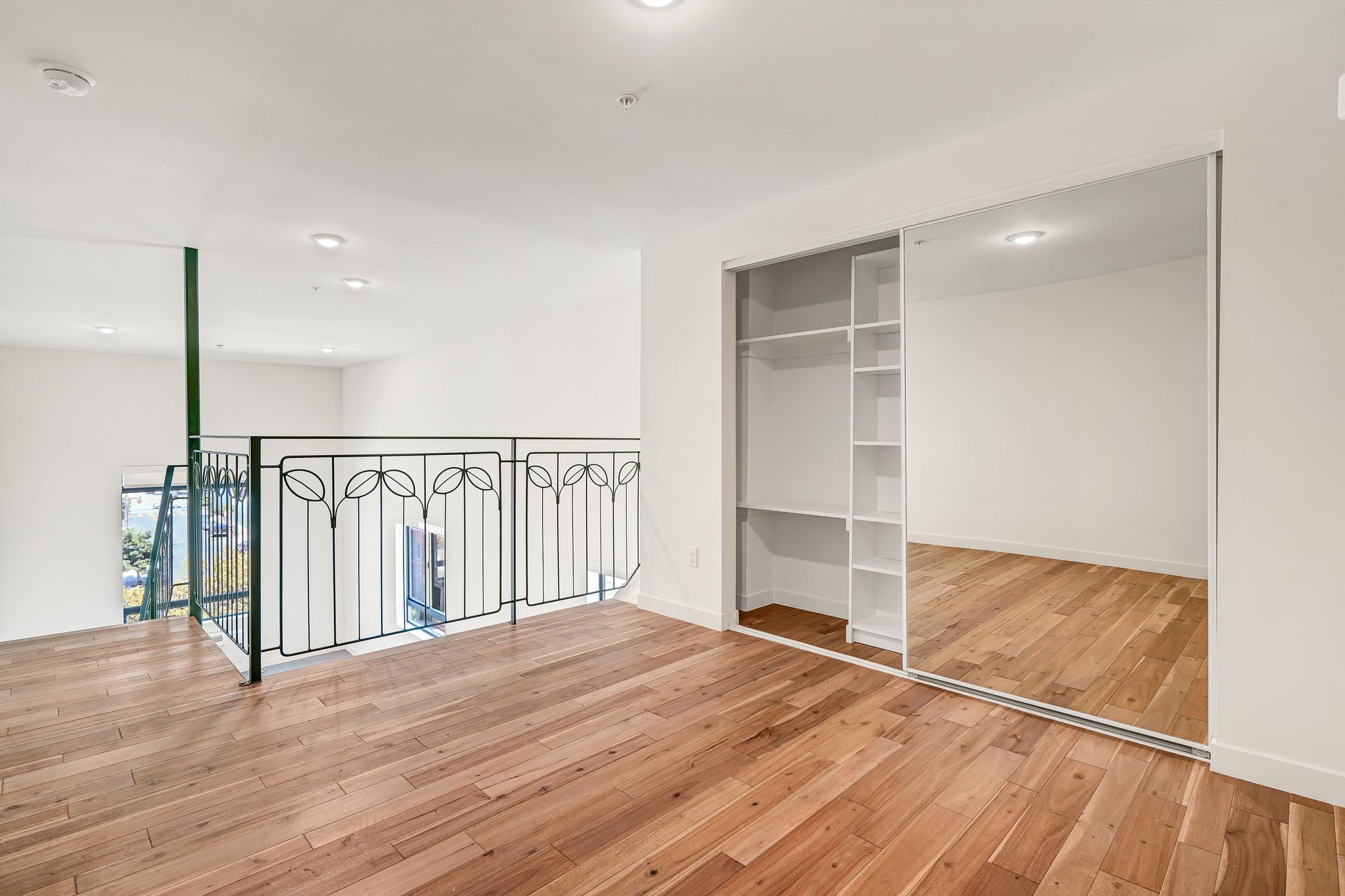 Loft bedroom with hardwood floors, a closet with mirrored sliding doors, and a wrought-iron railing.