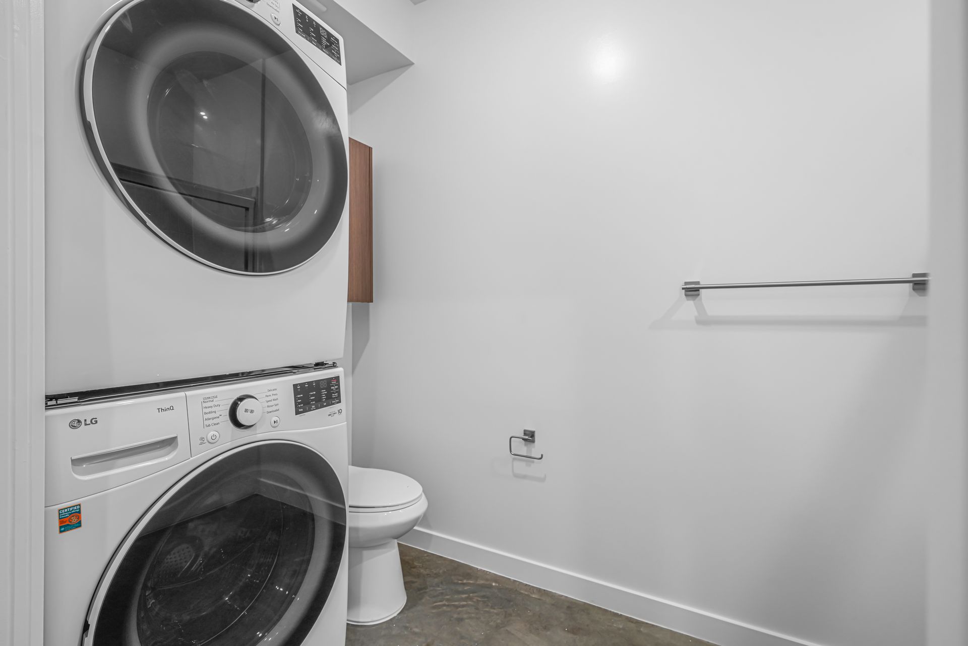 Stackable washer and dryer next to a toilet in a small, white laundry room.