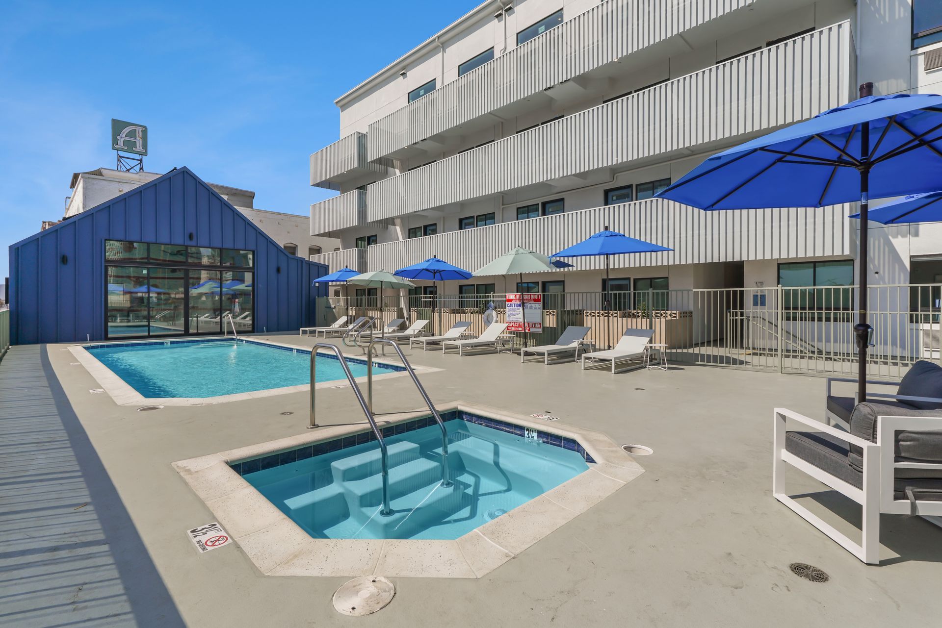 Pool and jacuzzi area at a modern hotel with blue umbrellas and lounge chairs.