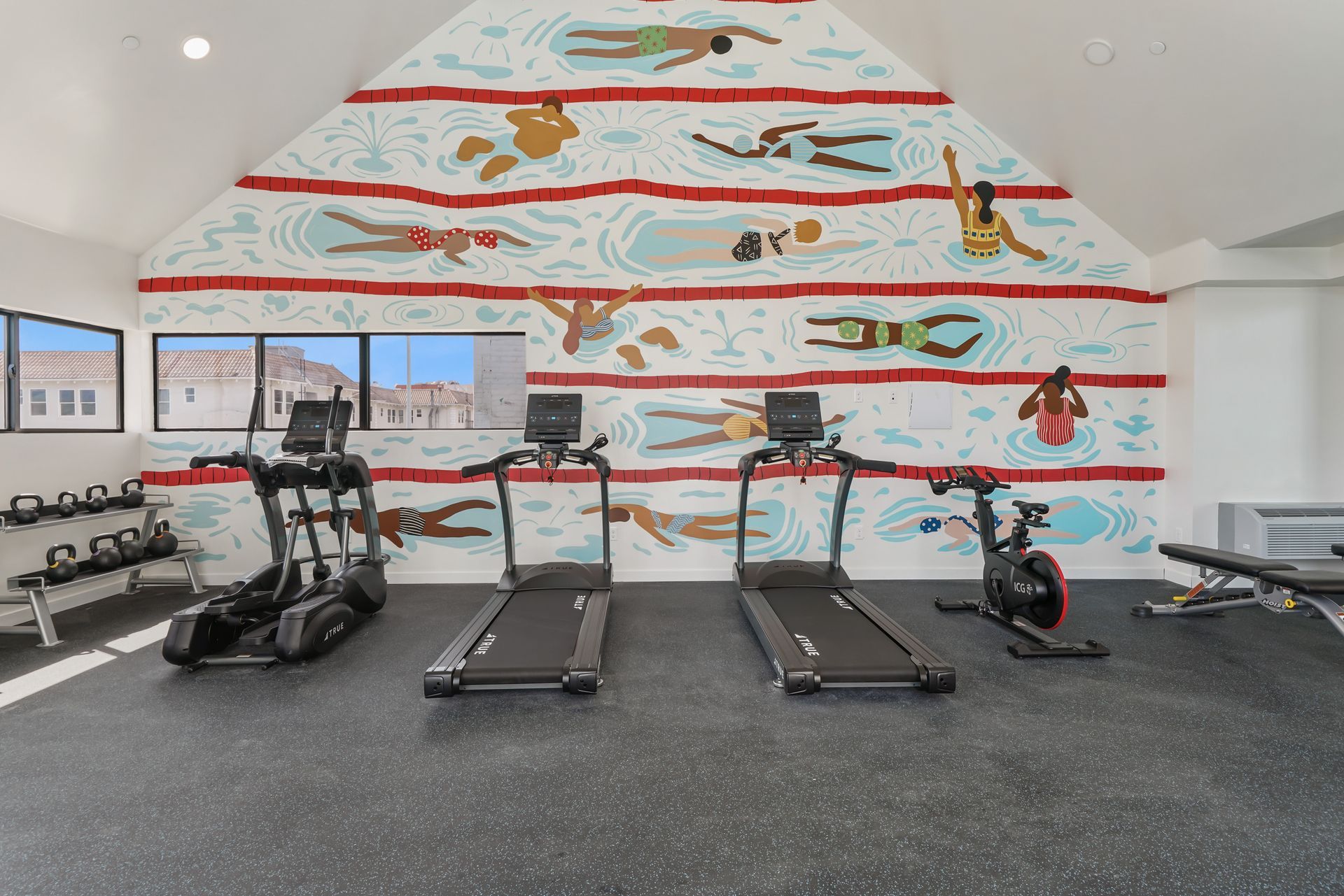 Gym with exercise equipment, swimmers mural on the wall, and cityscape view.