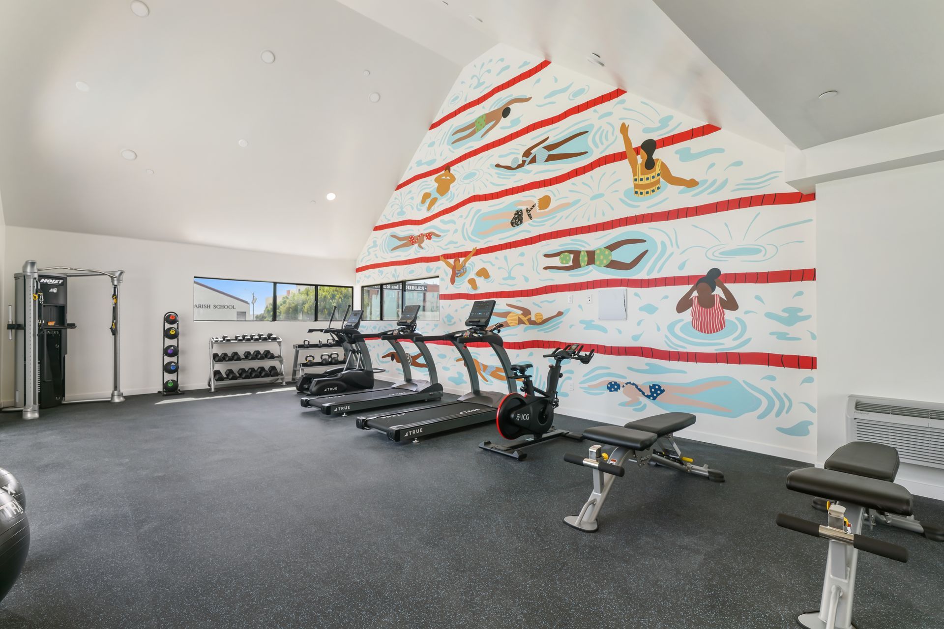 Gym with exercise equipment, including treadmills and weights, against a wall with a swimming mural.