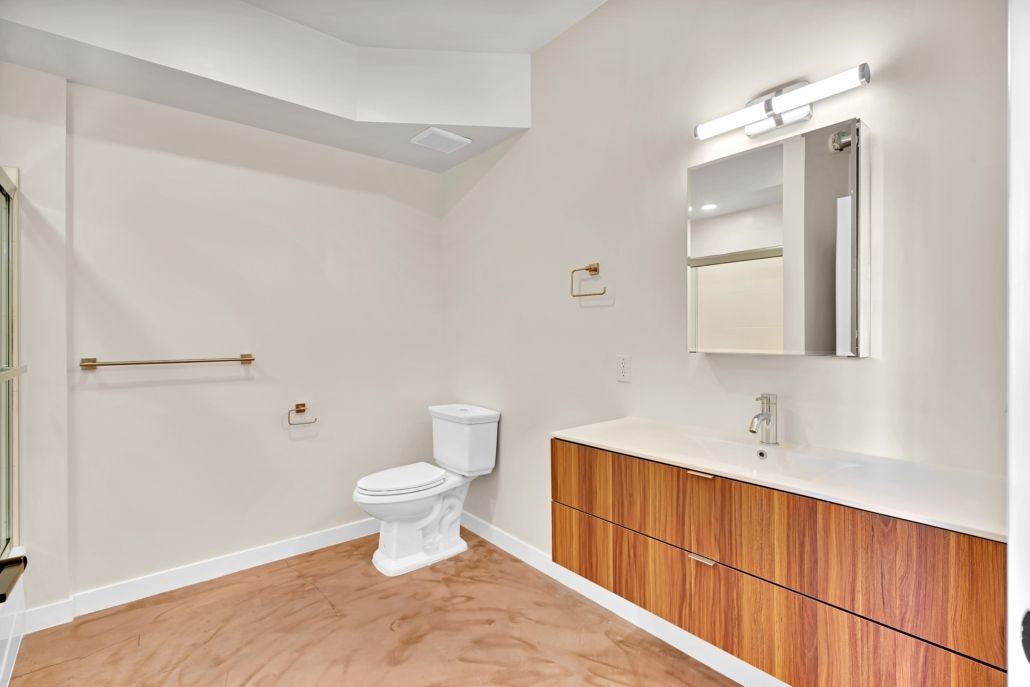 Empty modern bathroom with white walls, toilet, towel bar, mirror, and wood vanity cabinets