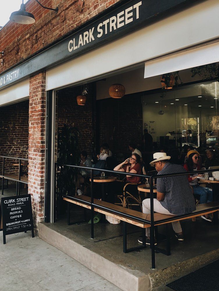 Clark Street cafe exterior with patrons seated at tables. Red brick wall, awning, and a chalkboard menu.
