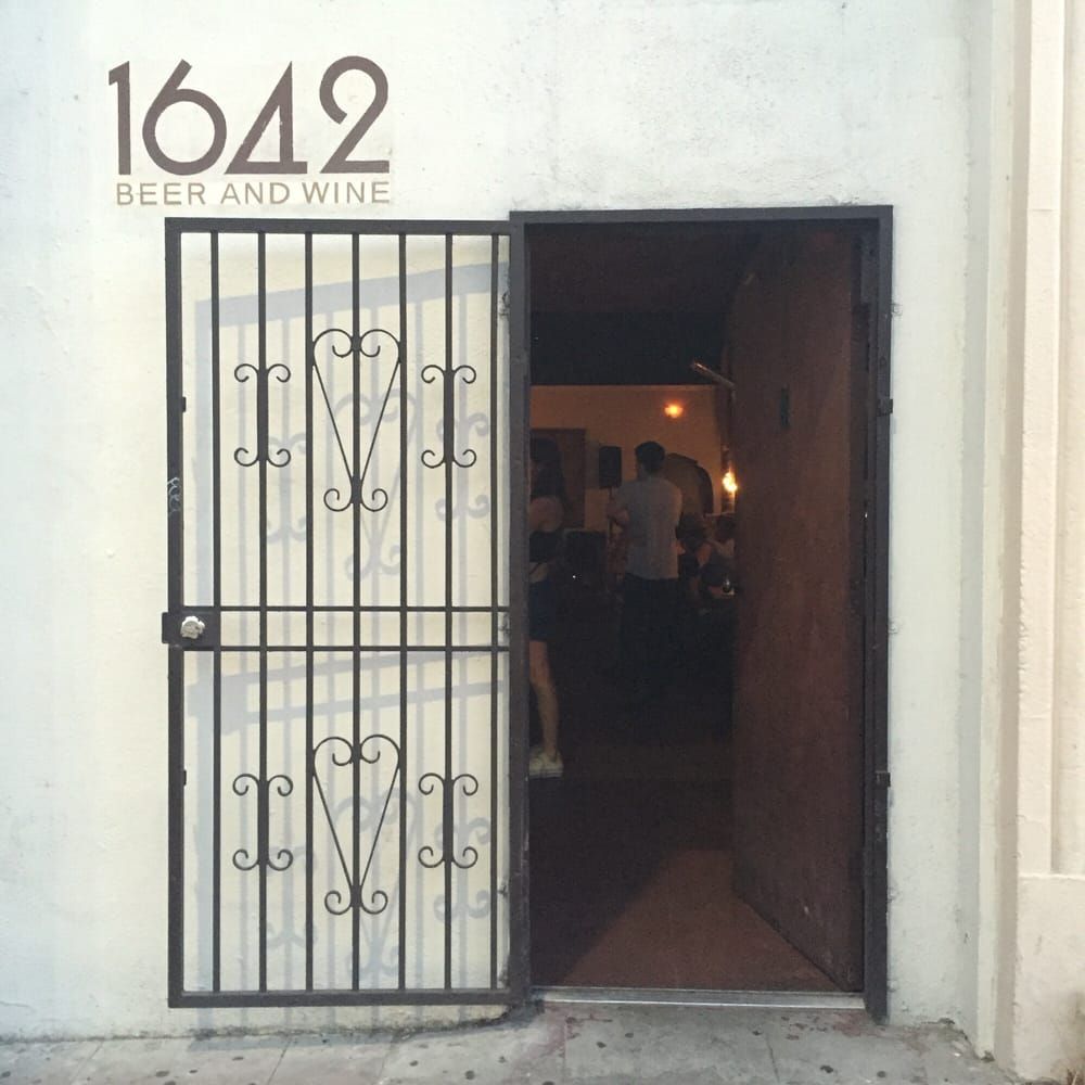 Exterior of 1642 Beer and Wine. Open doorway reveals people inside. A security gate is in front.