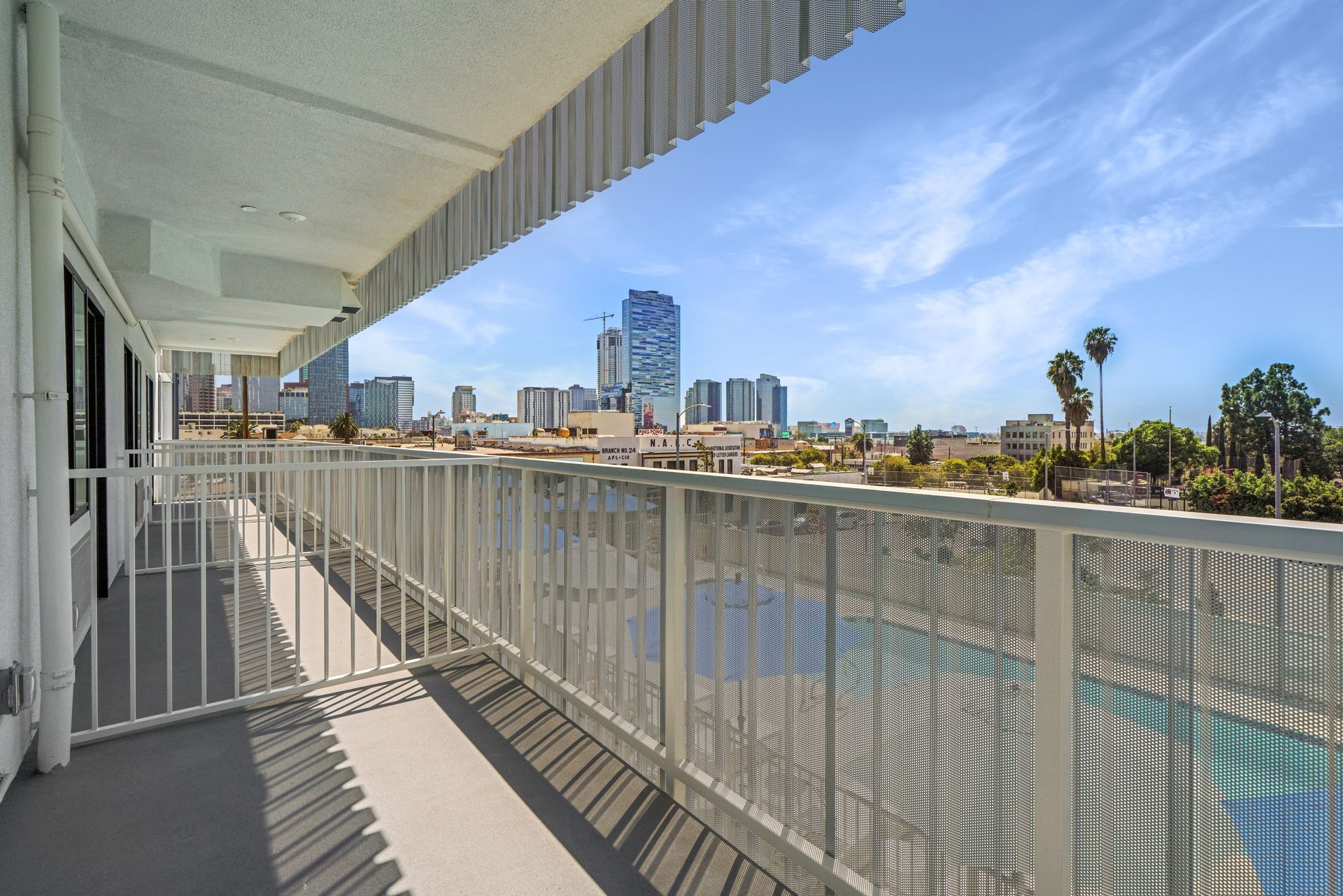 Balcony with white railing overlooking a city skyline and a swimming pool.