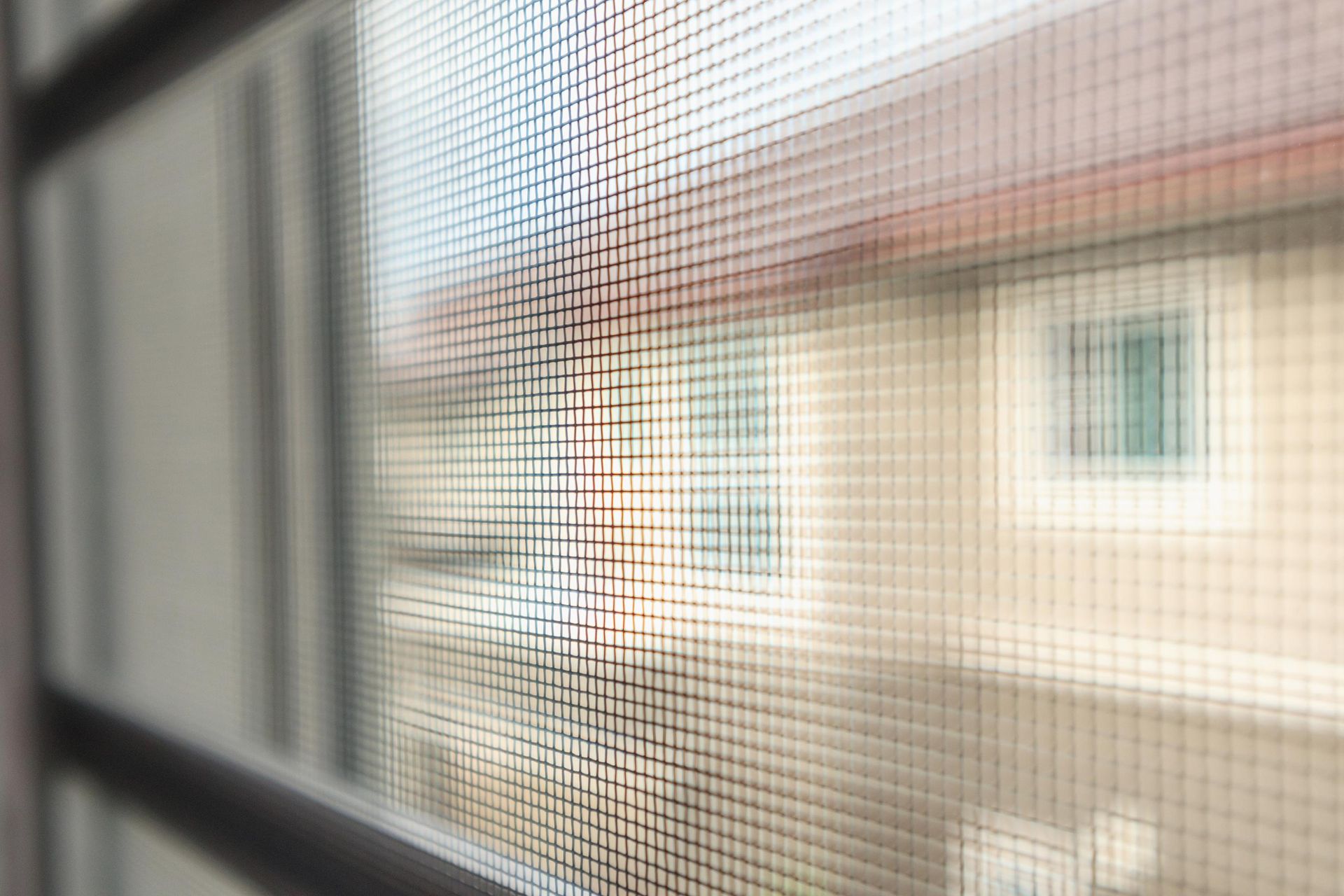Window screen, blurry view of buildings and sky through mesh.