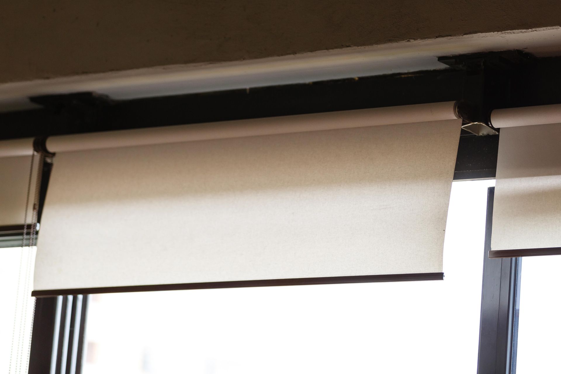 Off-white roller shade, partially lowered, inside a window frame.
