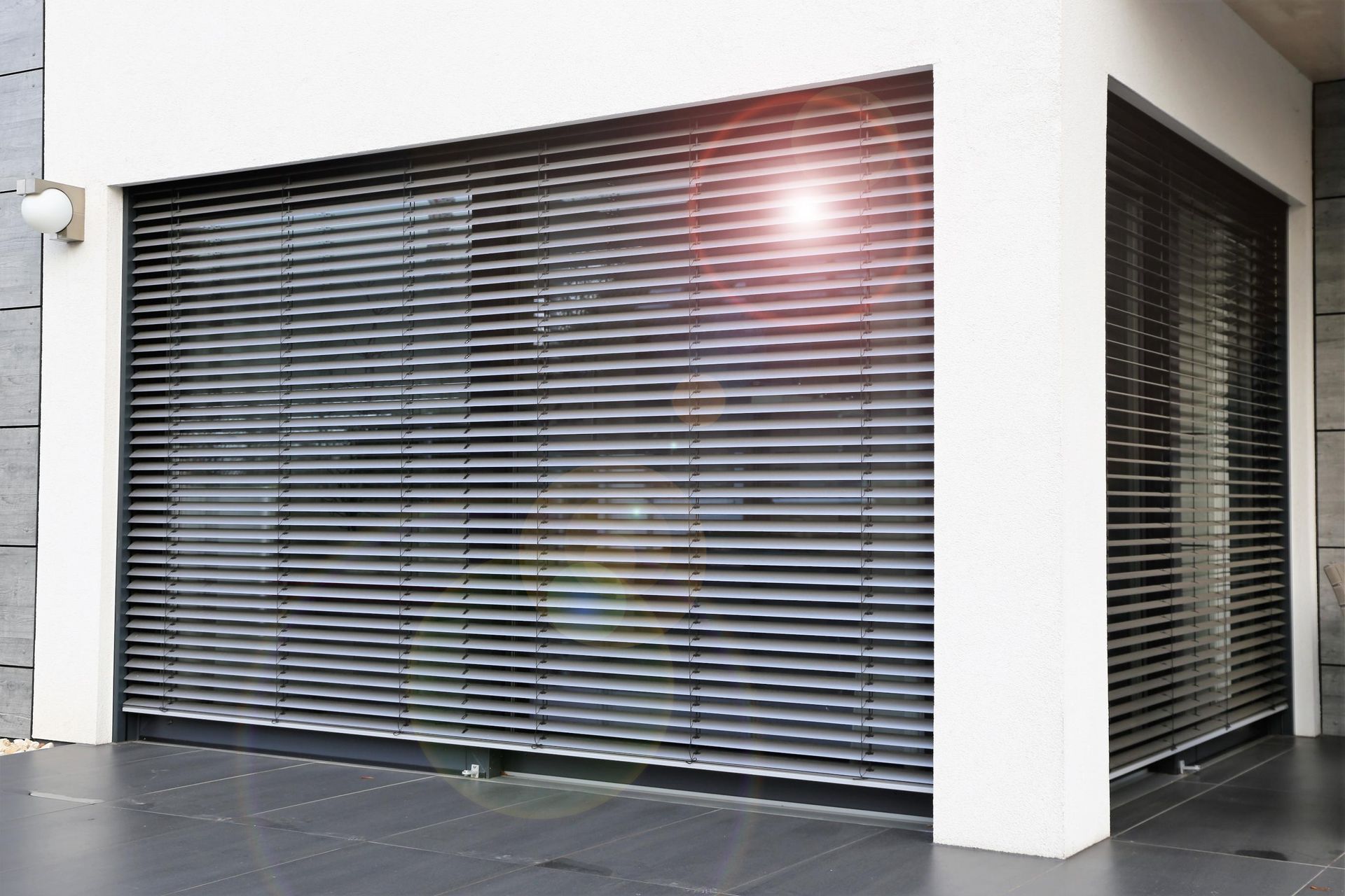 Gray metal security shutters covering a building's windows, a white wall, and gray floor.