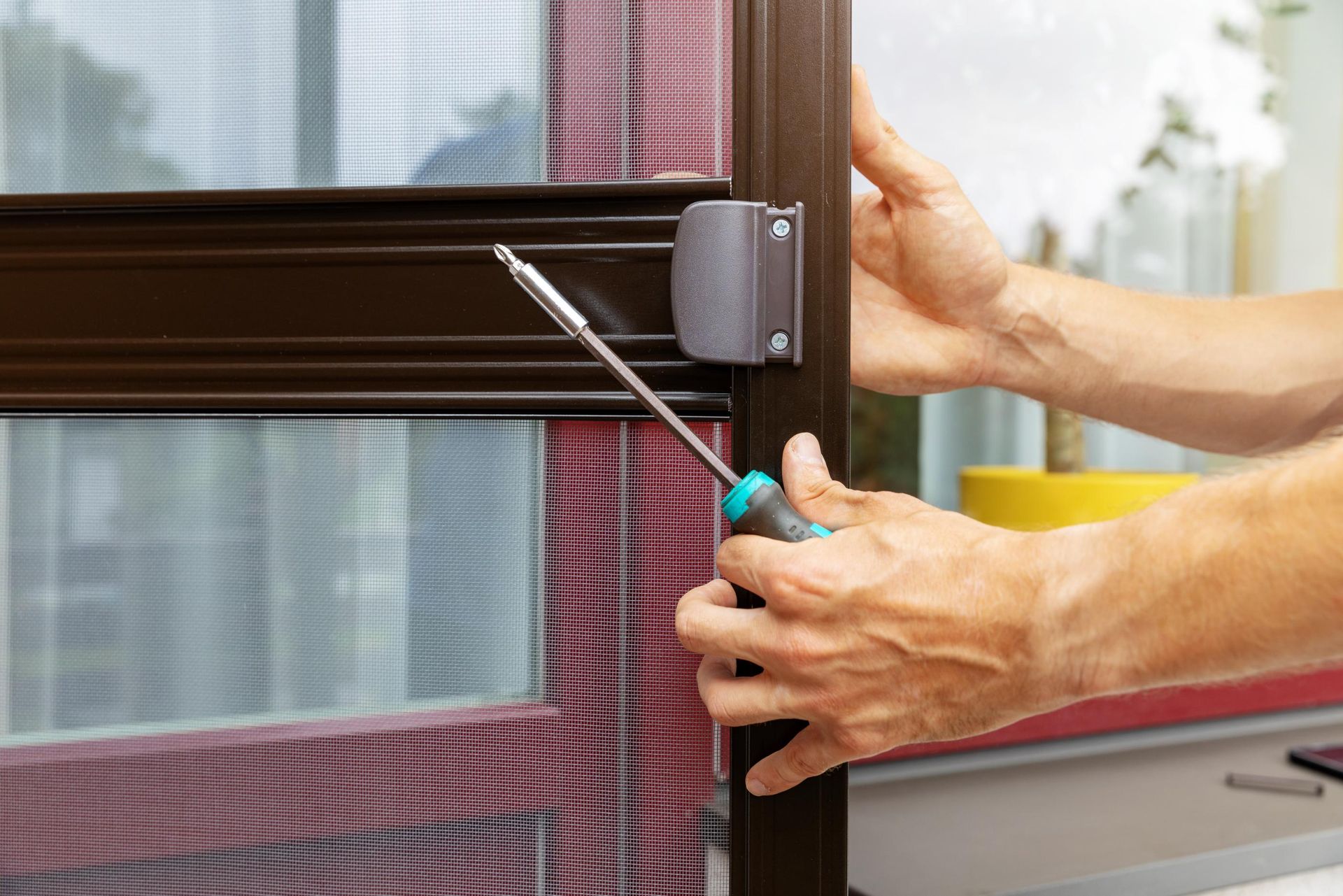 Person using a screwdriver to install a door latch on a brown metal frame next to a window.