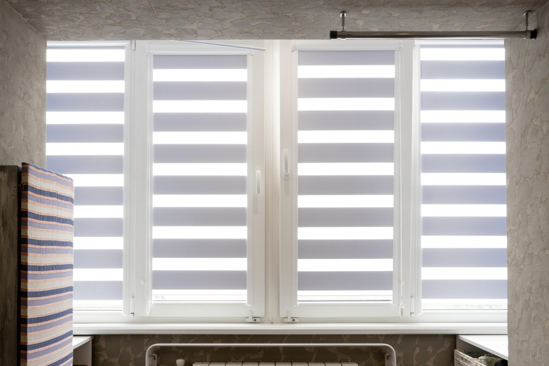 Window with gray and white striped blinds, in a room with light gray walls.