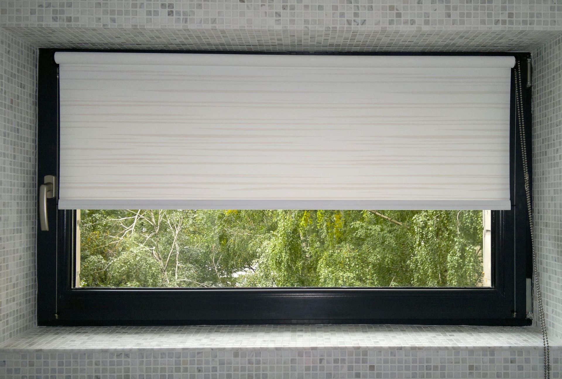 Window with closed white blinds overlooking green trees.