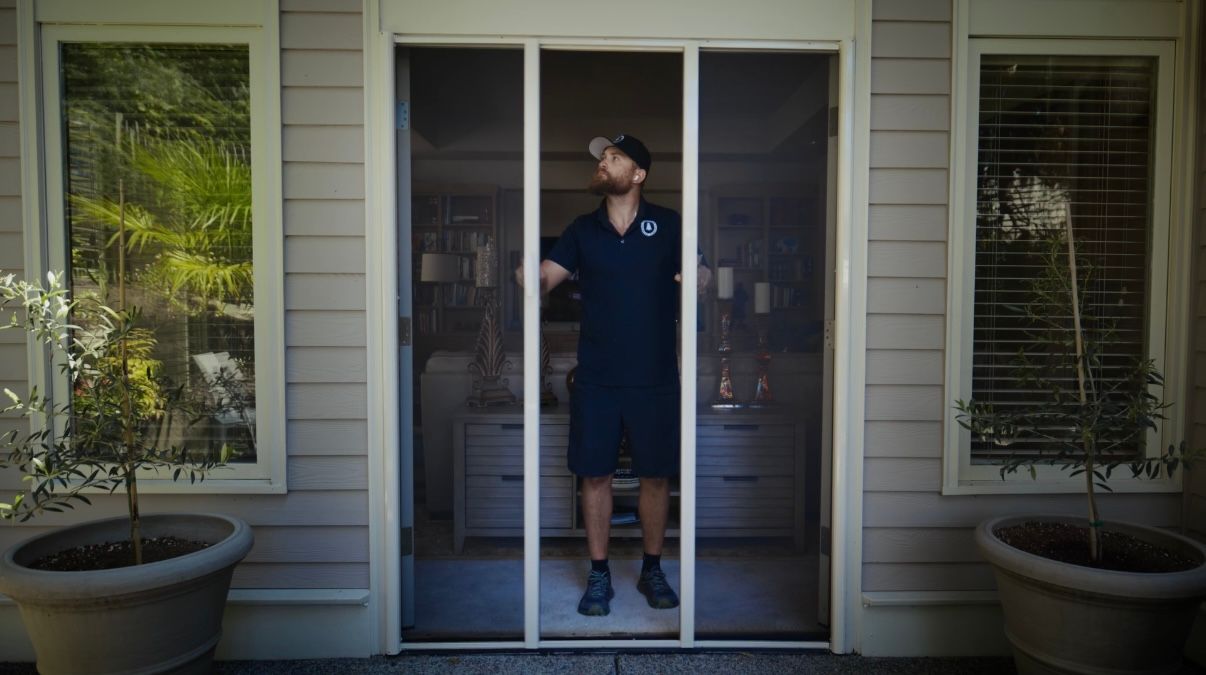 Person wearing gloves using a screwdriver to repair a sliding door, tools on the floor.