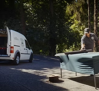 Man installing a window screen on a white-framed window, outdoors.