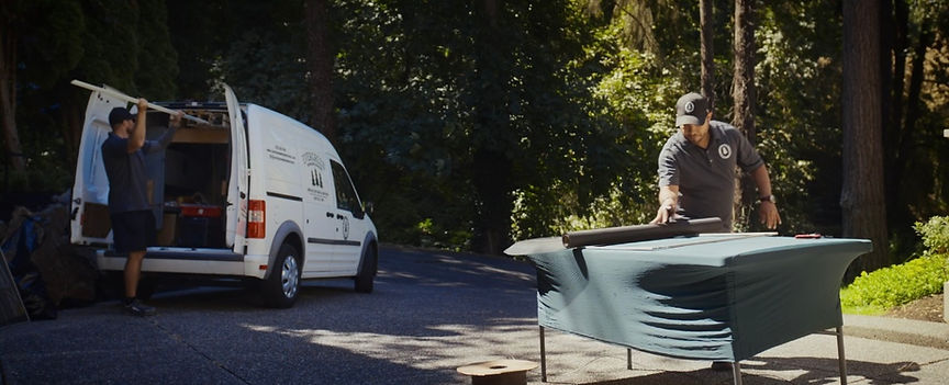 Two movers loading items from a van in front of a house. One sets up a table.