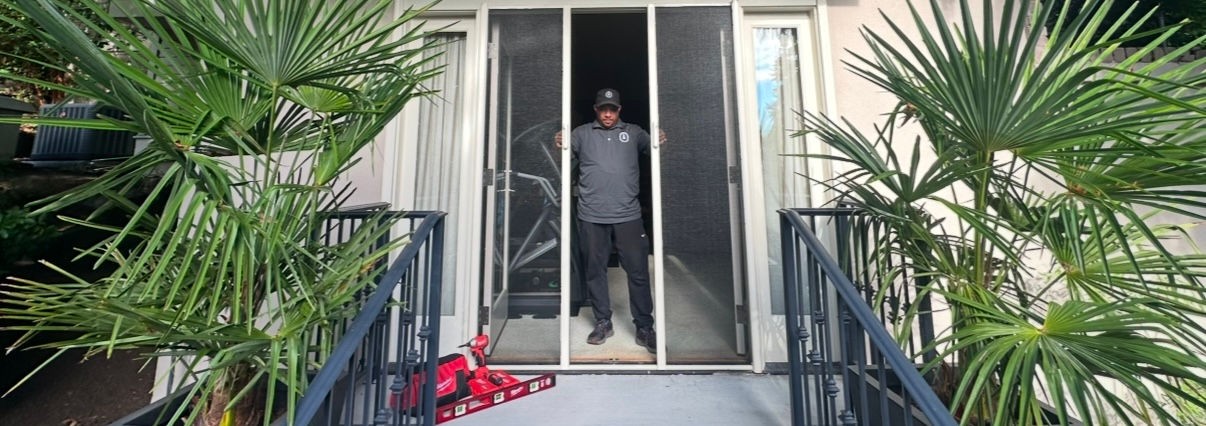 Man standing in a doorway with a screen door, palm trees and stairs on either side.