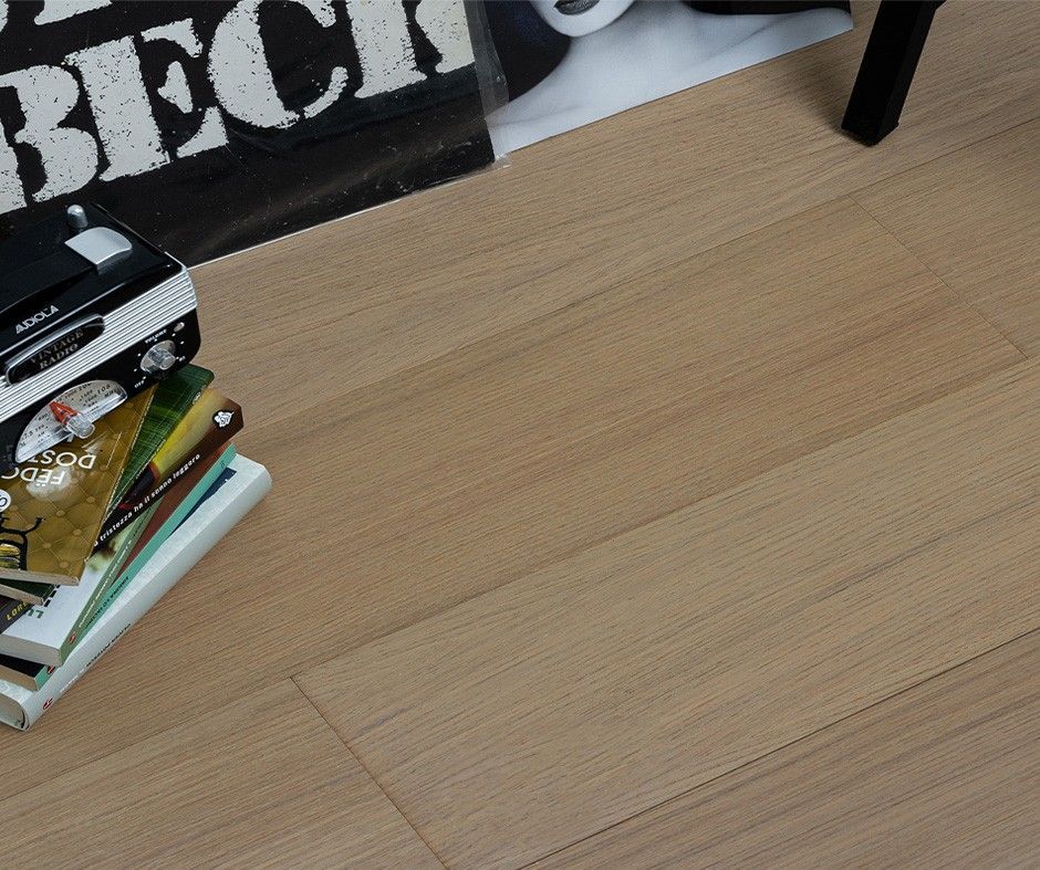 Pavimento in legno chiaro con oggetti: una pila di libri, un mangianastri d'epoca e un poster.